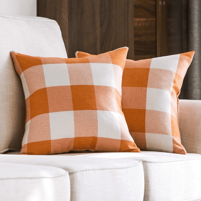 Two orange and white buffalo plaid throw pillows on a light beige sofa