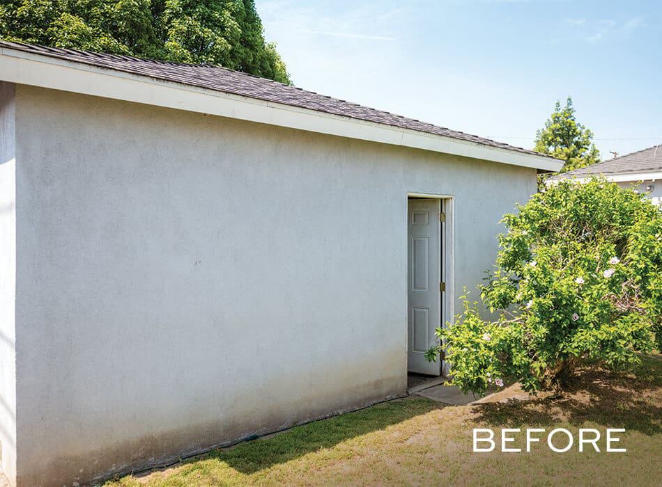 Plain outdoor storage shed with white walls, small door, and adjacent greenery