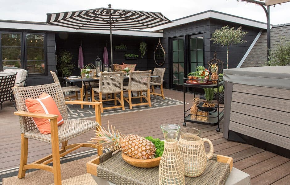 Outdoor deck with dining area, wicker furniture, and a striped umbrella near a hot tub