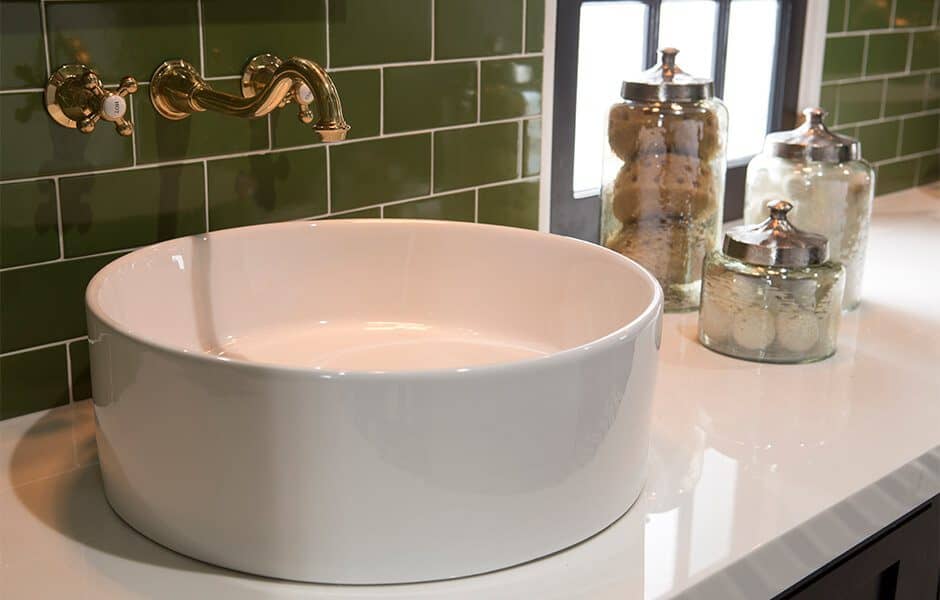 Bathroom with a round vessel sink, brass wall-mounted faucet, and green subway tile backsplash