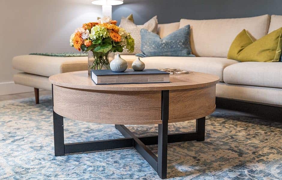 Living room with a round wooden coffee table decorated with flowers and books in front of a beige sectional sofa