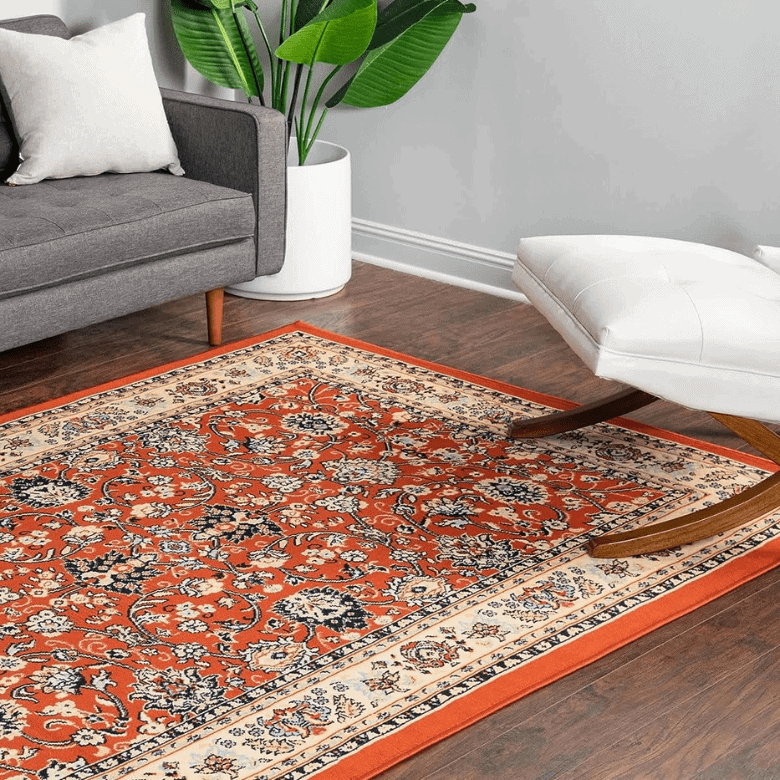 Living room corner with patterned red area rug, gray sofa, white lounge chair, and potted plant