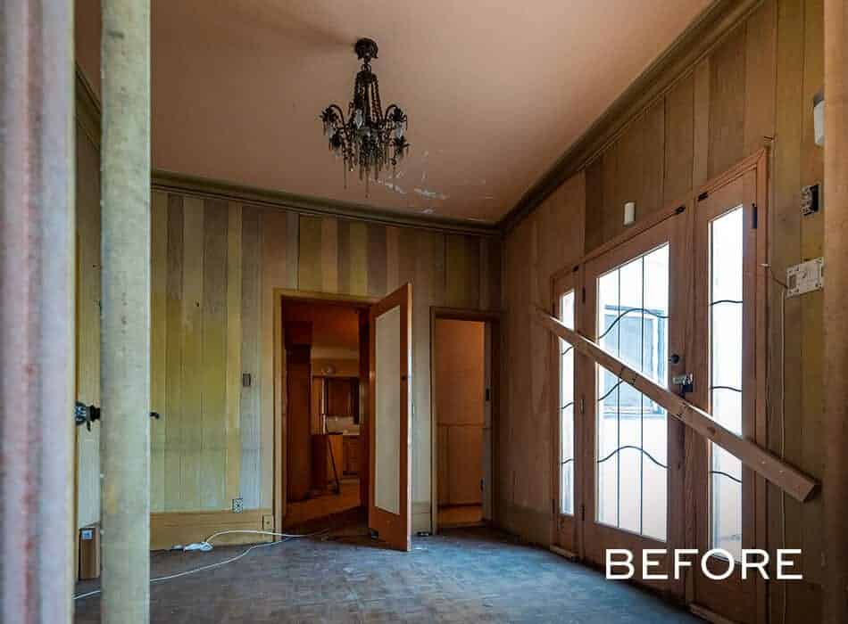 Room with wood-paneled walls, a chandelier, and French doors, shown in a worn condition before renovation