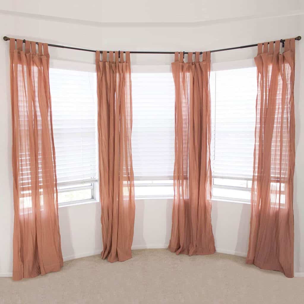 Bay window with sheer blush-colored curtains on a curved curtain rod