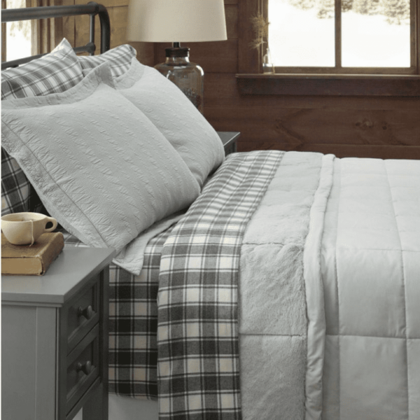 Cozy bed with gray plaid bedding, soft pillows, and a wooden wall backdrop
