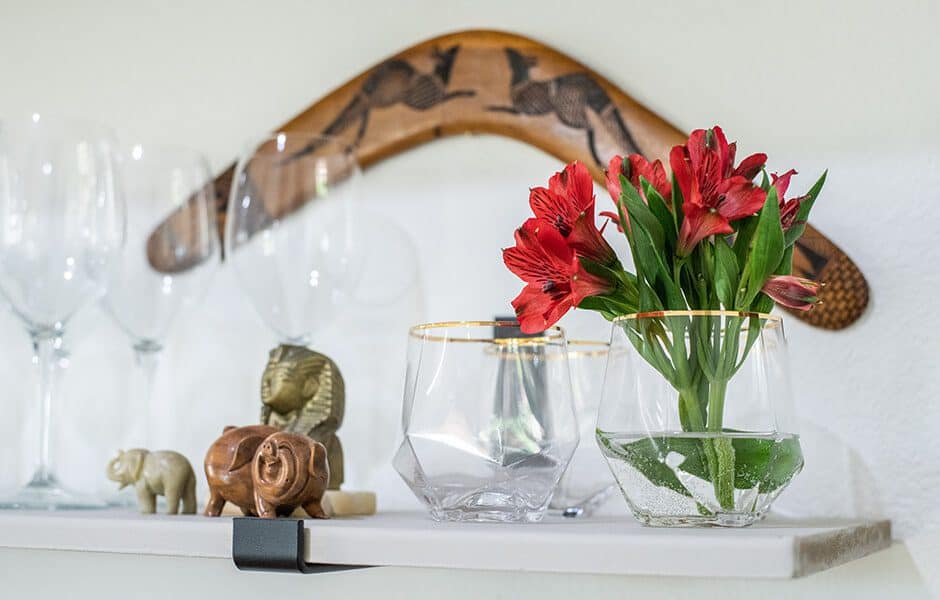 Decorative shelf with glassware, red flowers, and wooden figurines