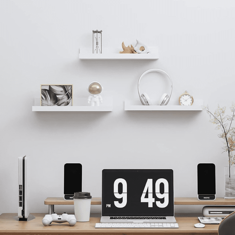 Minimalist desk setup with floating shelves, laptop, speakers, and a gaming console
