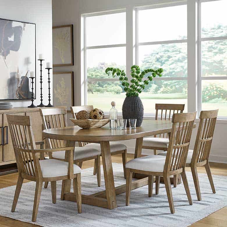 Dining room with wooden table, six matching chairs, black vase centerpiece, and large windows