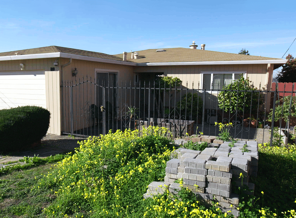 Single-story beige house with a brown roof, a white garage door, and a metal fence