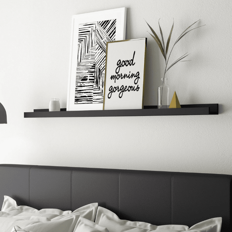 Black floating shelf above bed with framed artwork vase and decor against white wall