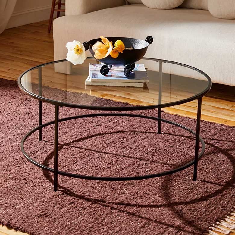 Glass coffee table with a black metal frame, a decorative bowl, and books on a brown rug