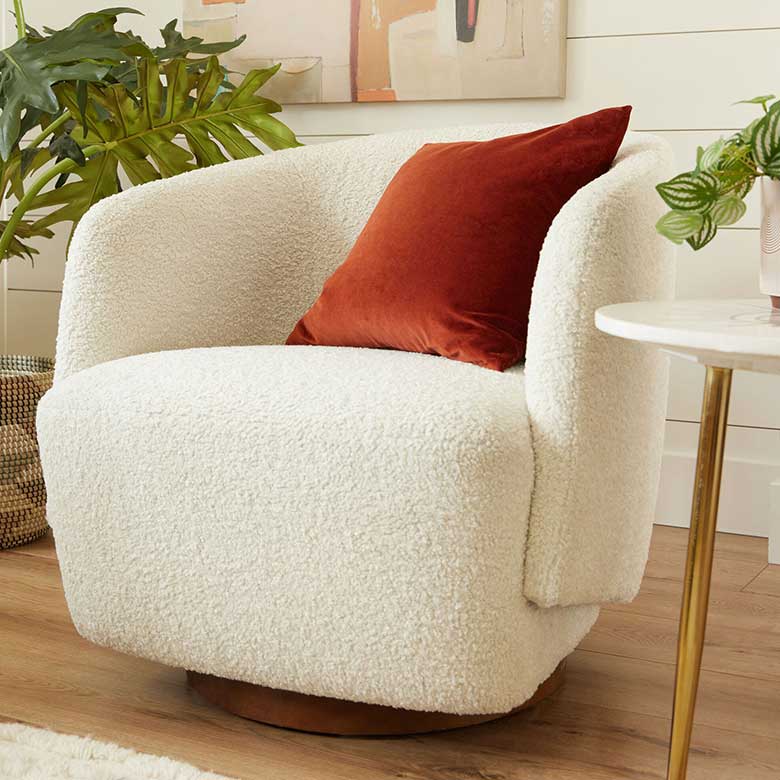 White boucle chair with rust-colored pillow and modern side table