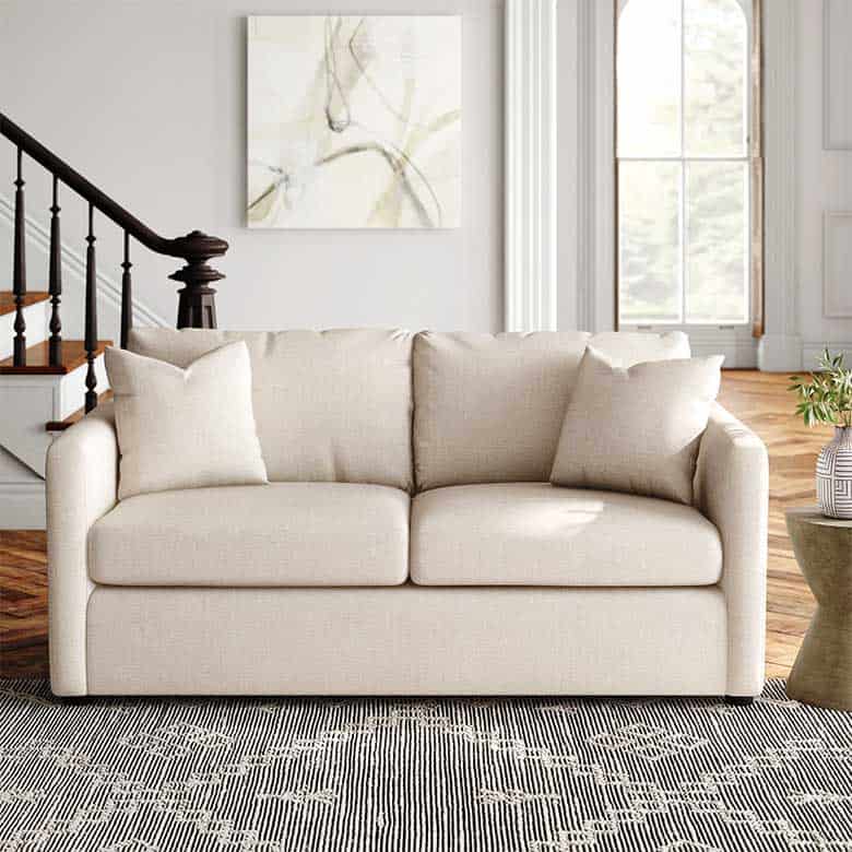 Neutral-colored sofa with two cushions, placed on a patterned rug in a bright, spacious living room