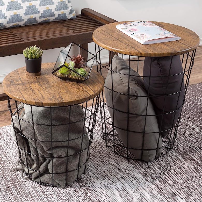 Two wire basket side tables with wood tops, one holding pillows and the other with succulents