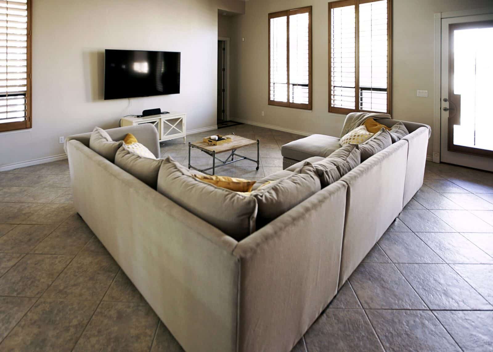 Spacious living room with a large sectional sofa, wall-mounted TV, and natural light from tall windows