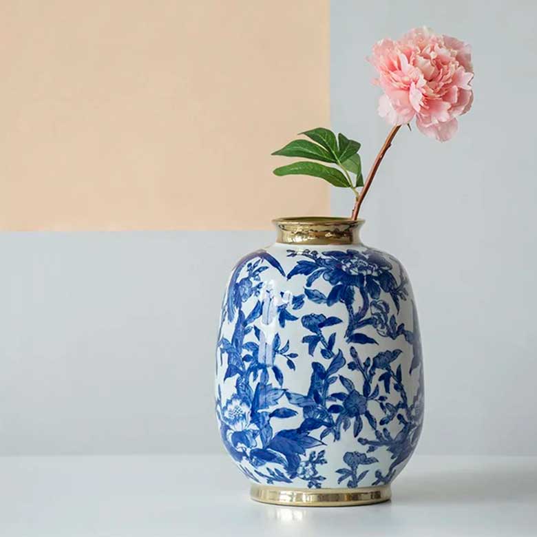 Blue and white floral vase with gold accents, holding a pink flower