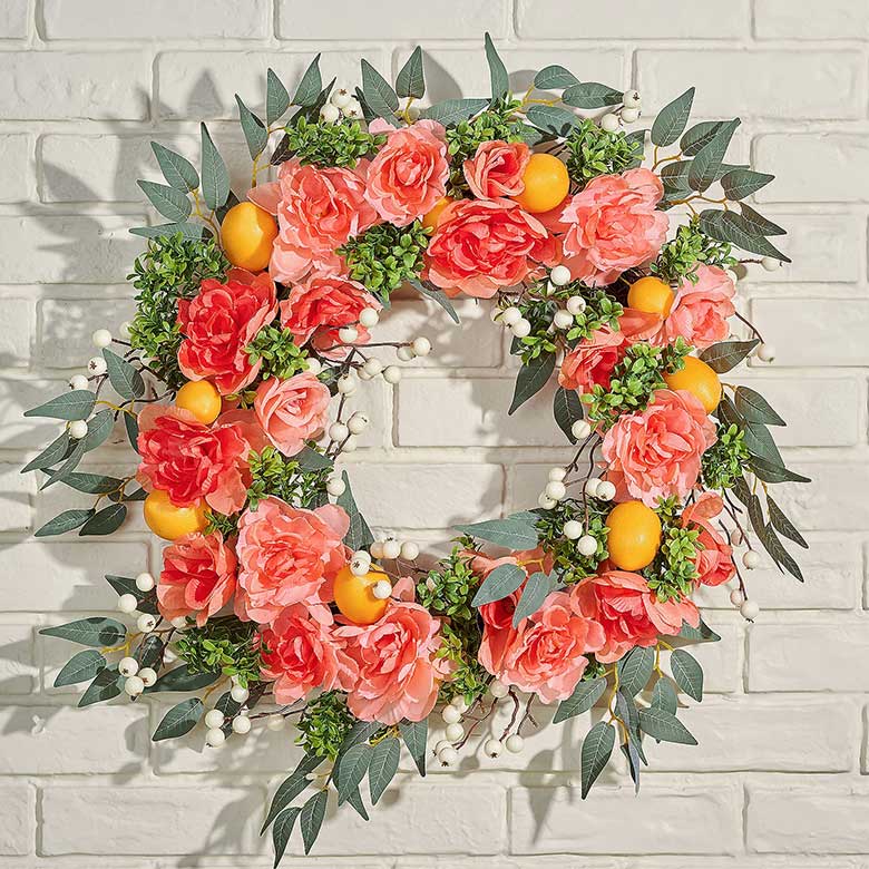 Floral wreath with pink roses, green leaves, white berries, and small orange fruits on a white brick wall