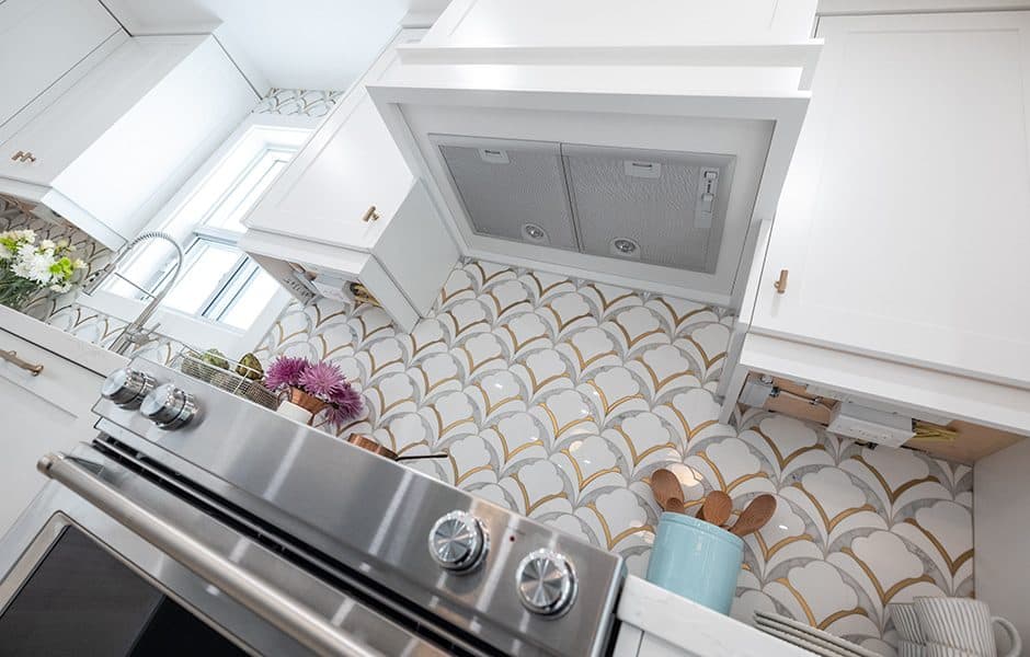 Kitchen with white cabinets, a stove, and a decorative backsplash made from scalloped, gold-trimmed tiles