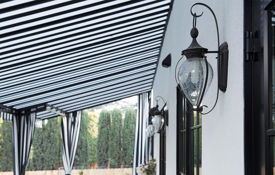 Modern outdoor patio with black and white striped awning glass lantern wall sconces and tall greenery