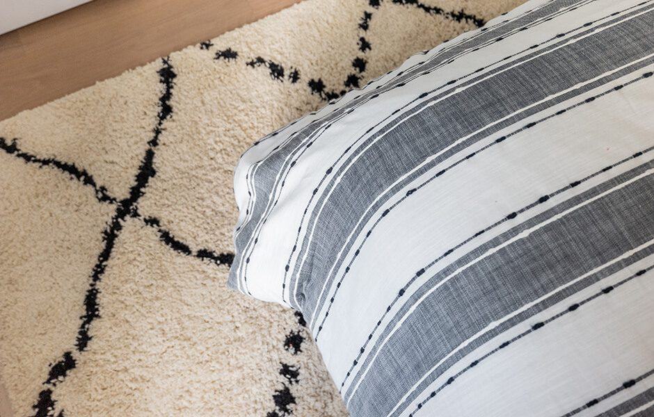 Close-up of a striped pillow on a textured, cream-colored rug with a black geometric pattern