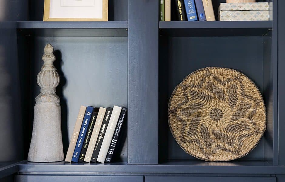 Navy blue bookshelf with stacked books, a decorative stone finial, and a woven circular basket accent