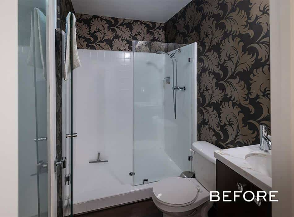 Bathroom with dark patterned wallpaper, a glass shower enclosure, white toilet, and vanity sink