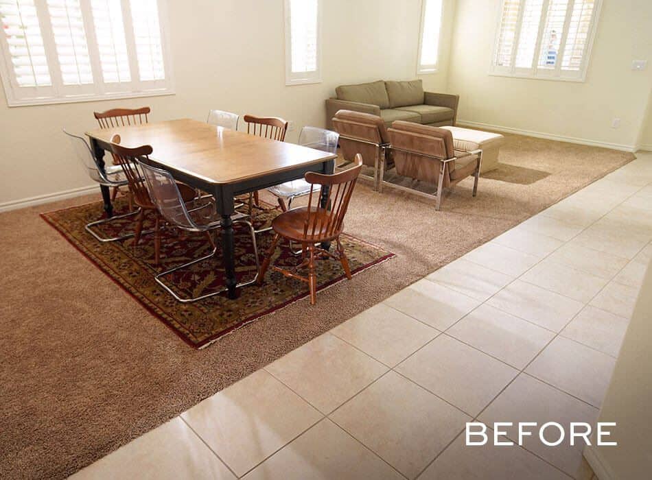 Simple dining and living space with beige carpeting, tile flooring, and basic furniture