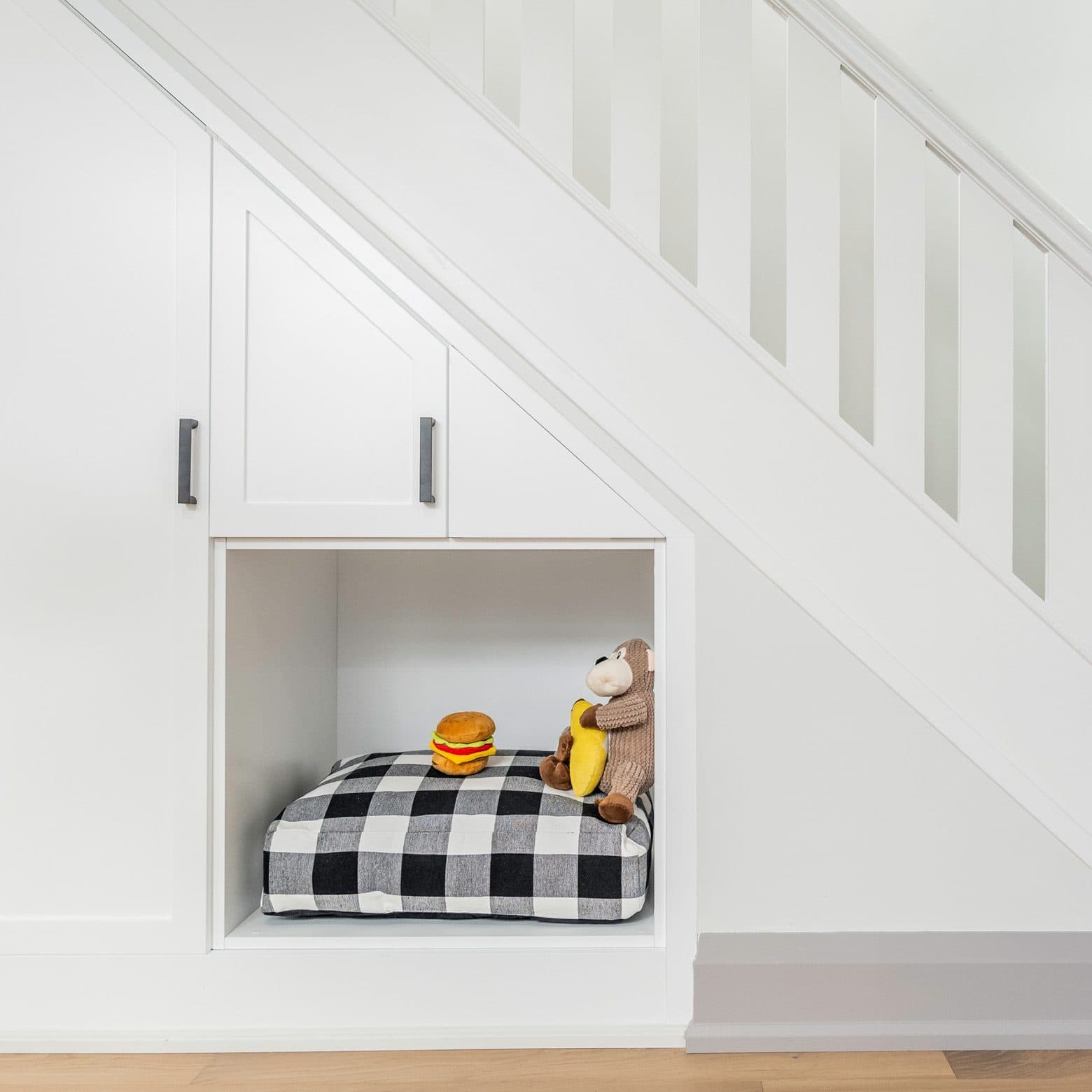 Built-in nook under stairs with buffalo plaid pet bed and stuffed toys