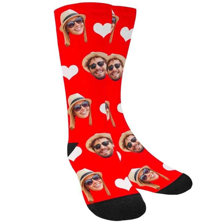 Red socks with black toes and heels, decorated with white hearts and printed faces of a man and woman wearing sunglasses and hats