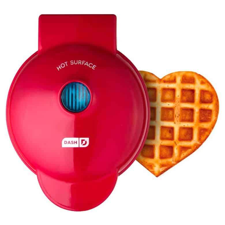 Red Dash waffle maker with a heart-shaped waffle beside it