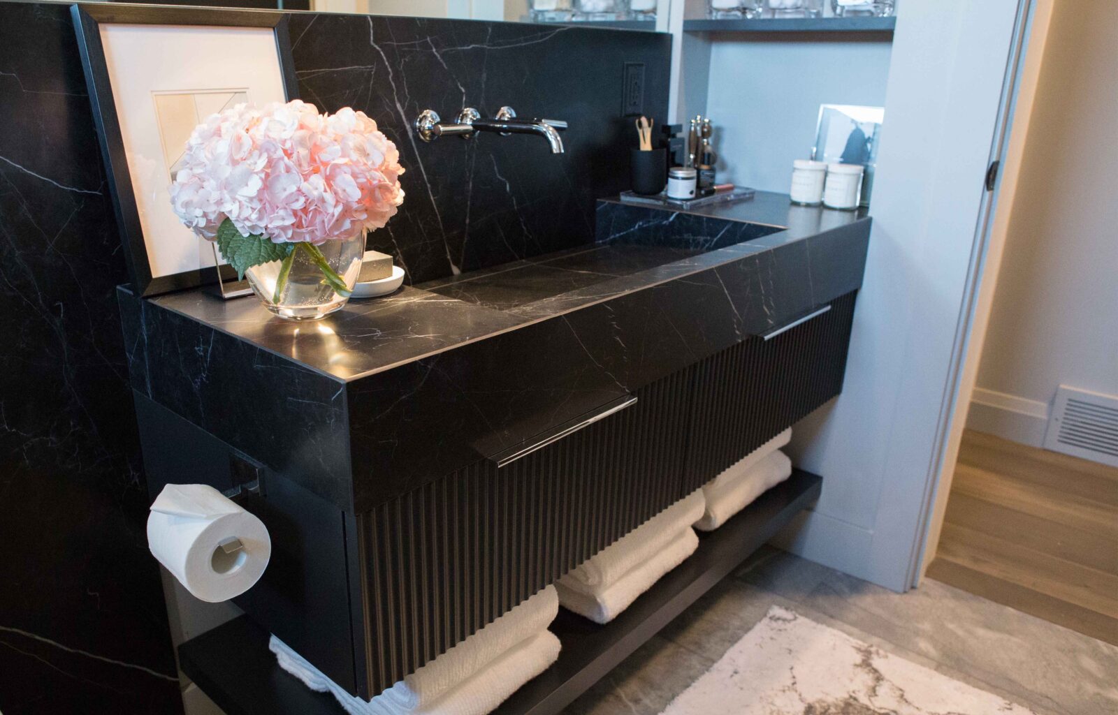 Black marble bathroom vanity with wall-mounted faucet, pink flowers, and stacked white towels
