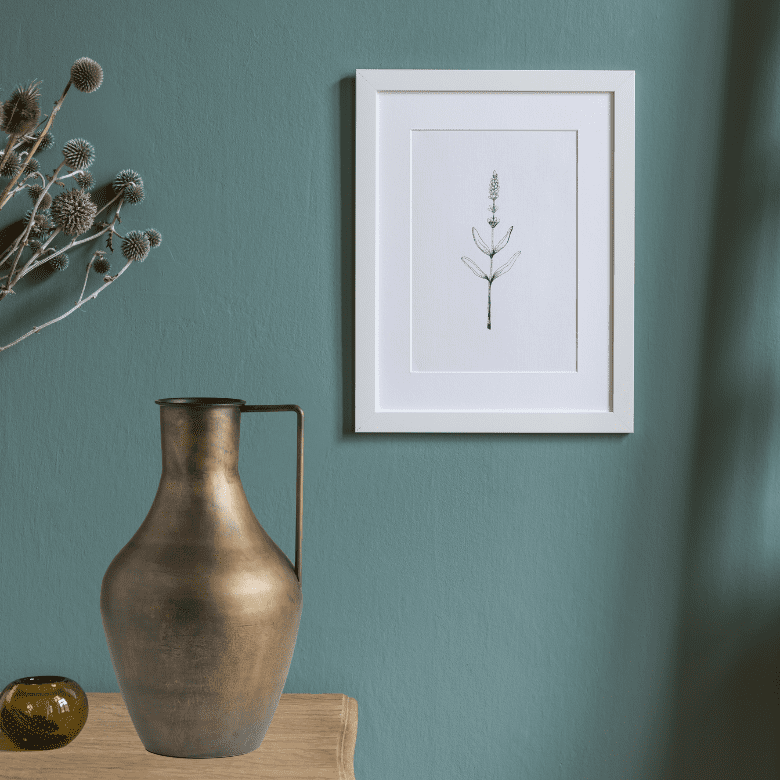 Minimal wall decor with botanical art, dried flowers, and a bronze pitcher on a wood surface
