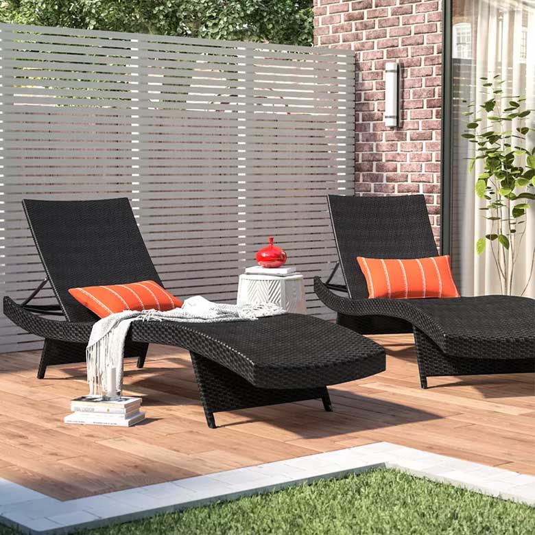 Outdoor patio with two black wicker lounge chairs, orange cushions, a white side table, and a privacy screen