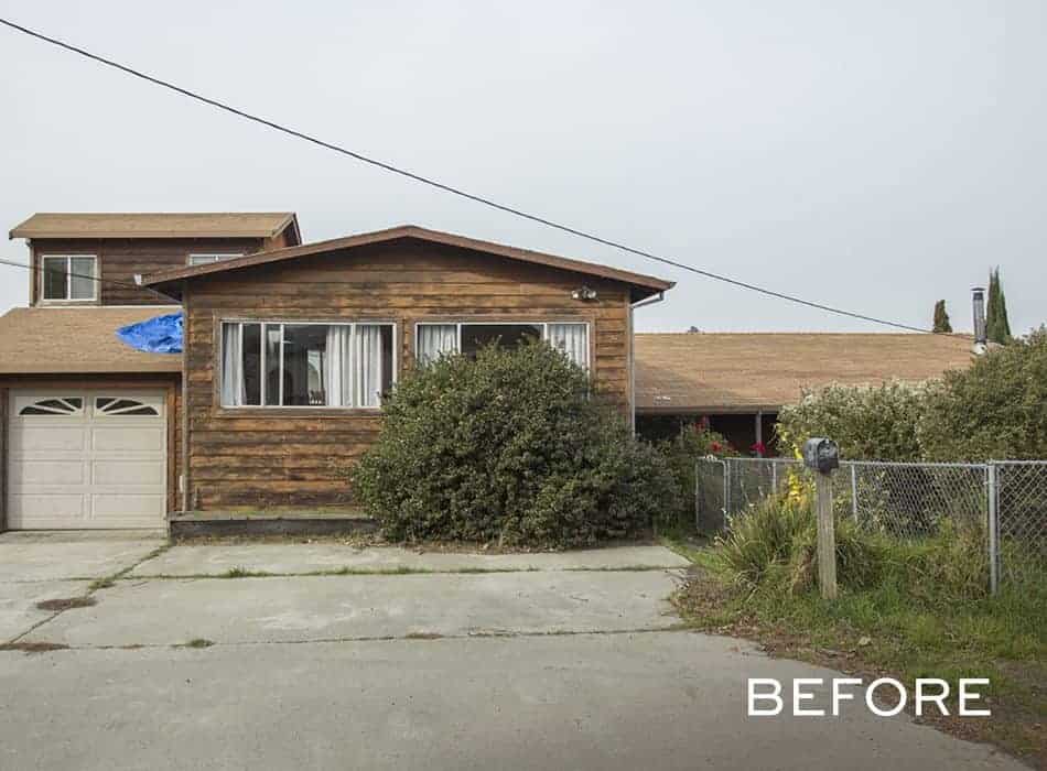 Old wooden house exterior with overgrown bushes, chain-link fence, and driveway