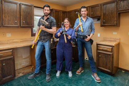 Three people standing in a dated kitchen holding renovation tools, ready for a remodel project