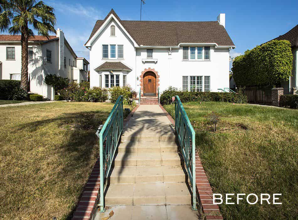 White two-story house with a brown roof, a brick walkway, and overgrown grass before renovation