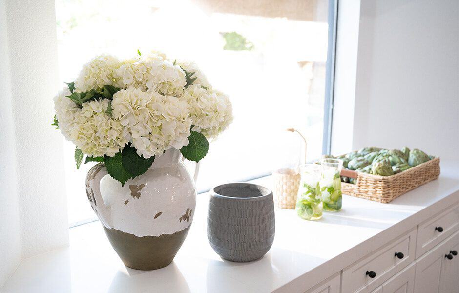 White hydrangea bouquet in ceramic vase with basket of artichokes and fresh drinks