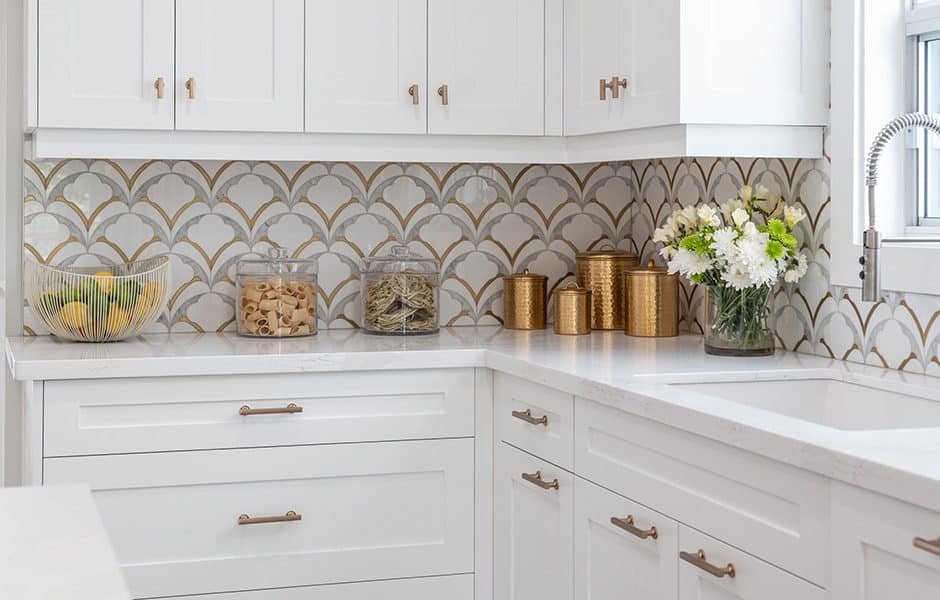 White kitchen with gold-accented backsplash, brass hardware, and decorative jars on the countertop