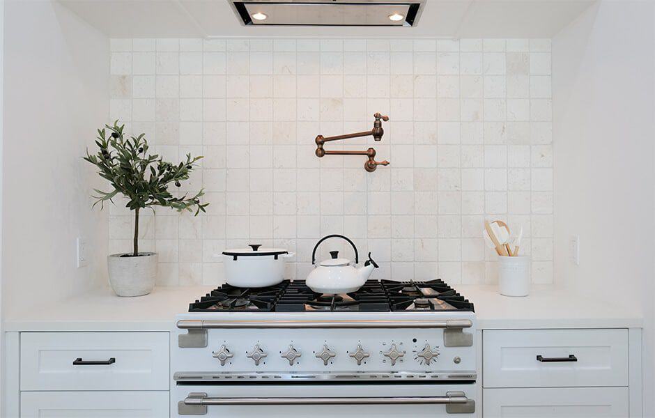 White stove with vintage design, tiled backsplash, pot filler, white kettle, and decorative plant