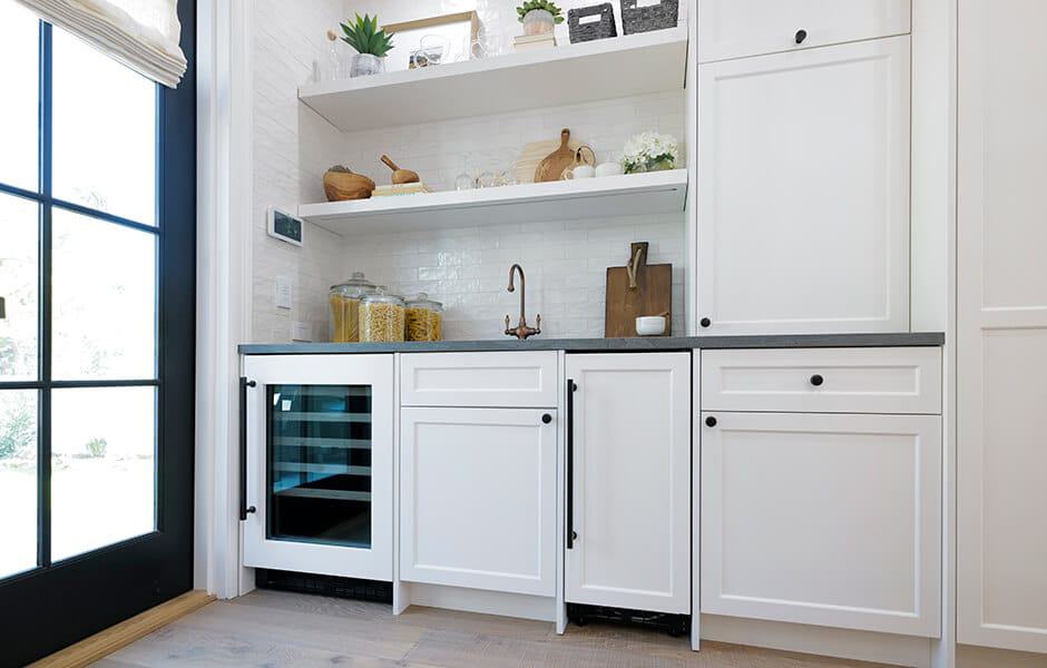 Modern white kitchen with shaker cabinets, black countertops, open shelves, and a small beverage fridge