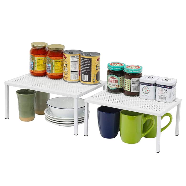 White metal kitchen shelf organizers holding jars, cans, mugs, and plates