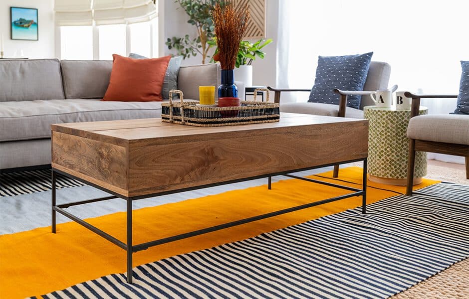 Wood and metal coffee table in a modern living room with colorful rugs, a gray sofa, and decorative accents