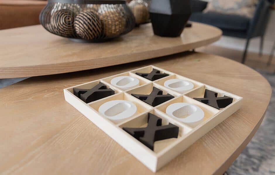 Wooden tic-tac-toe game with black X and white O pieces on a coffee table