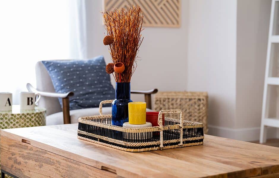 Decorative coffee table with a woven tray, dried floral arrangement, and colorful candles