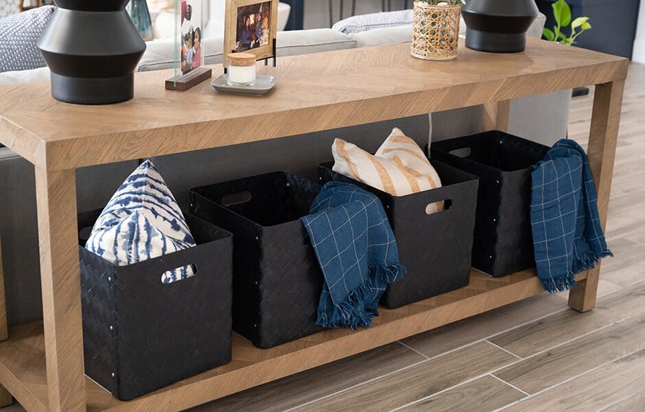 Wooden console table with black storage baskets holding pillows and throws, styled with decor on top