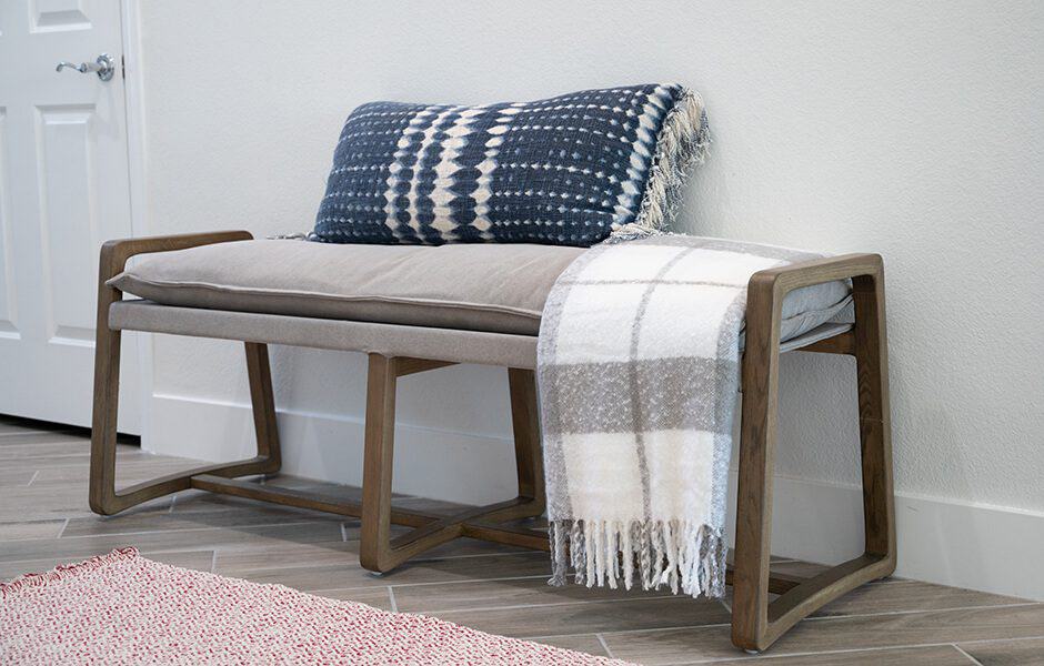 Wooden bench with a cushion, a patterned blue pillow, and a plaid throw blanket