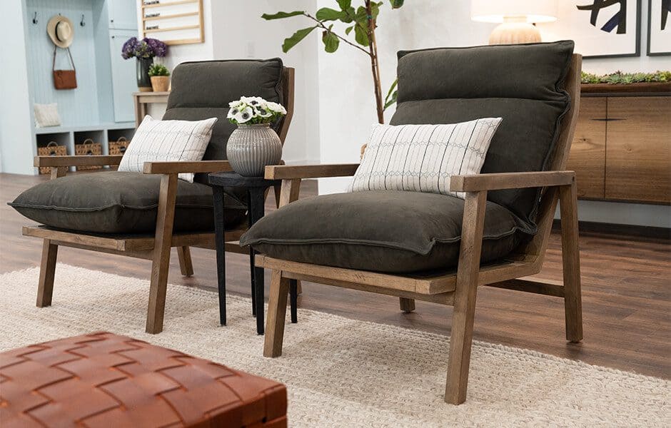 Two cushioned armchairs with wooden frames, separated by a small table with a vase, on a cozy rug in a living space