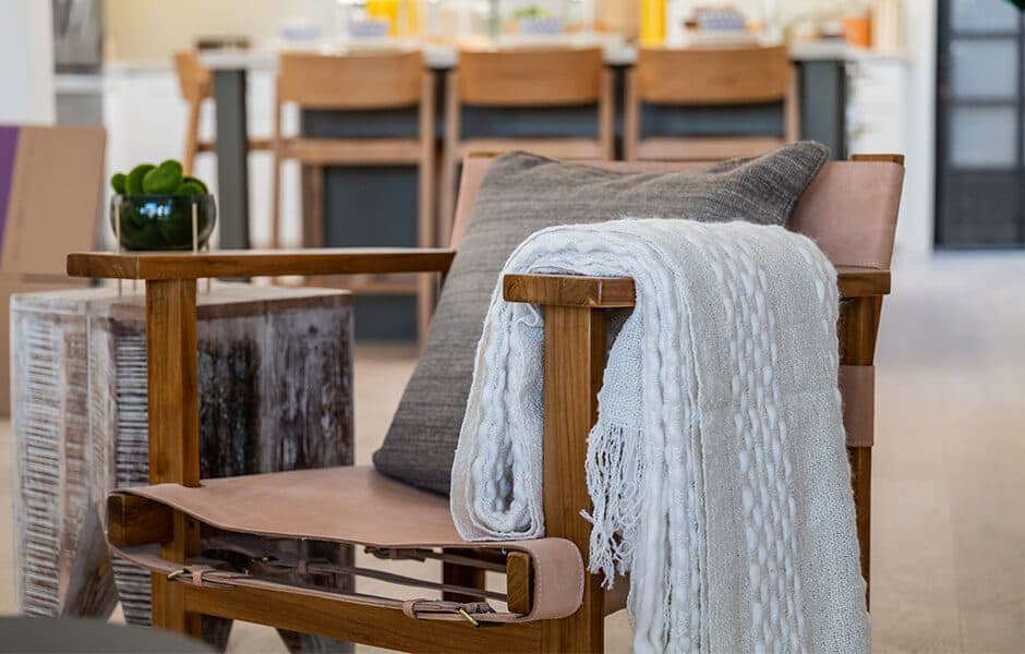 Wooden armchair with a gray pillow and a light knit throw draped over the side