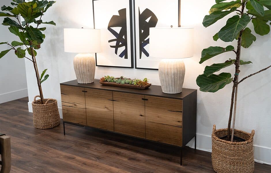 Sleek wooden console table with modern lamps and framed artwork, accented by potted fiddle-leaf figs