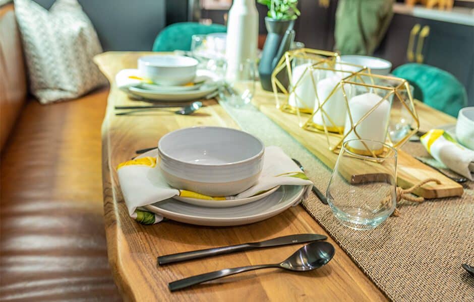 Dining table set with plates, bowls, utensils, glasses, and decorative candles on a wooden table